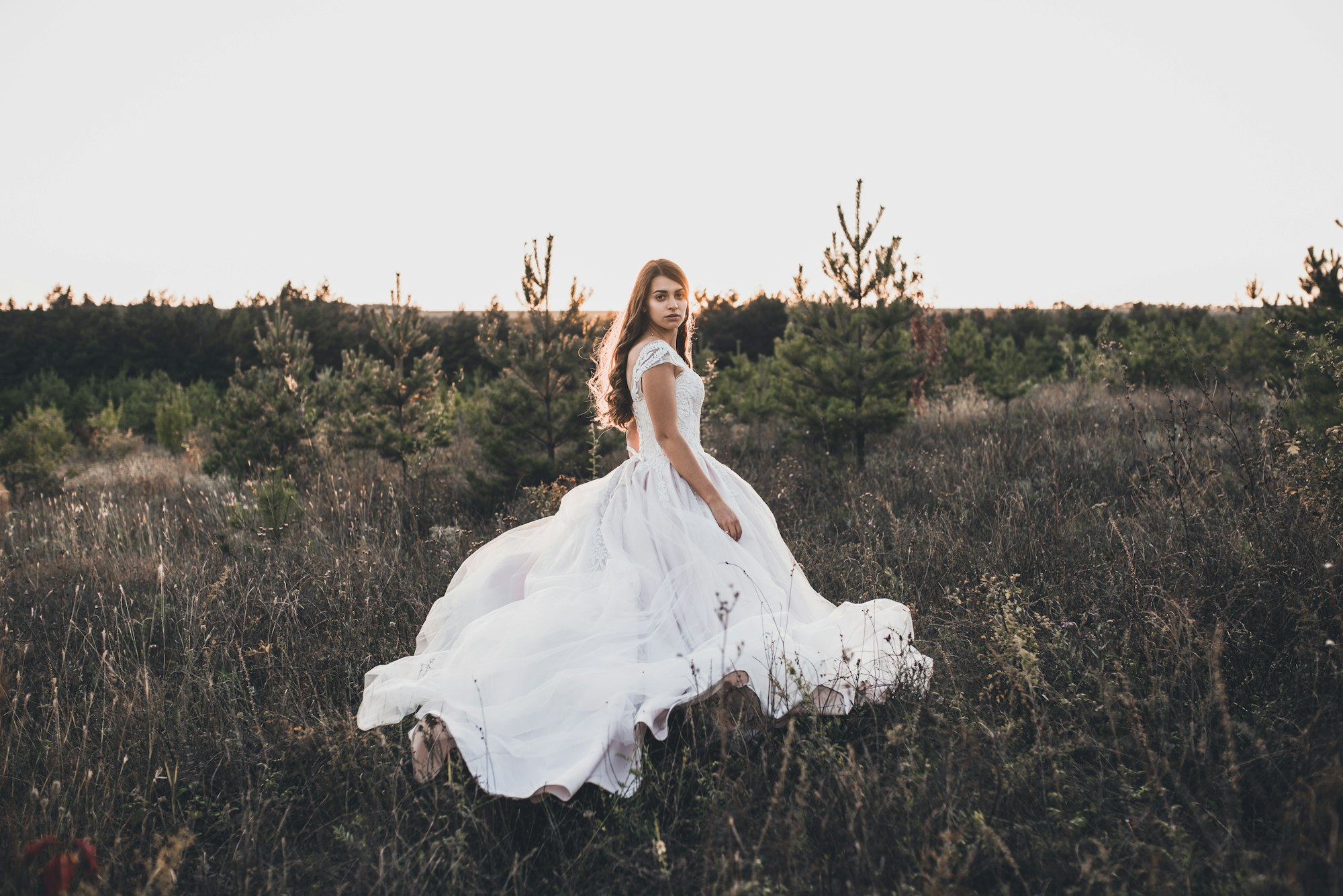 Bride in wedding white dress walking on meadow in summer at sunset