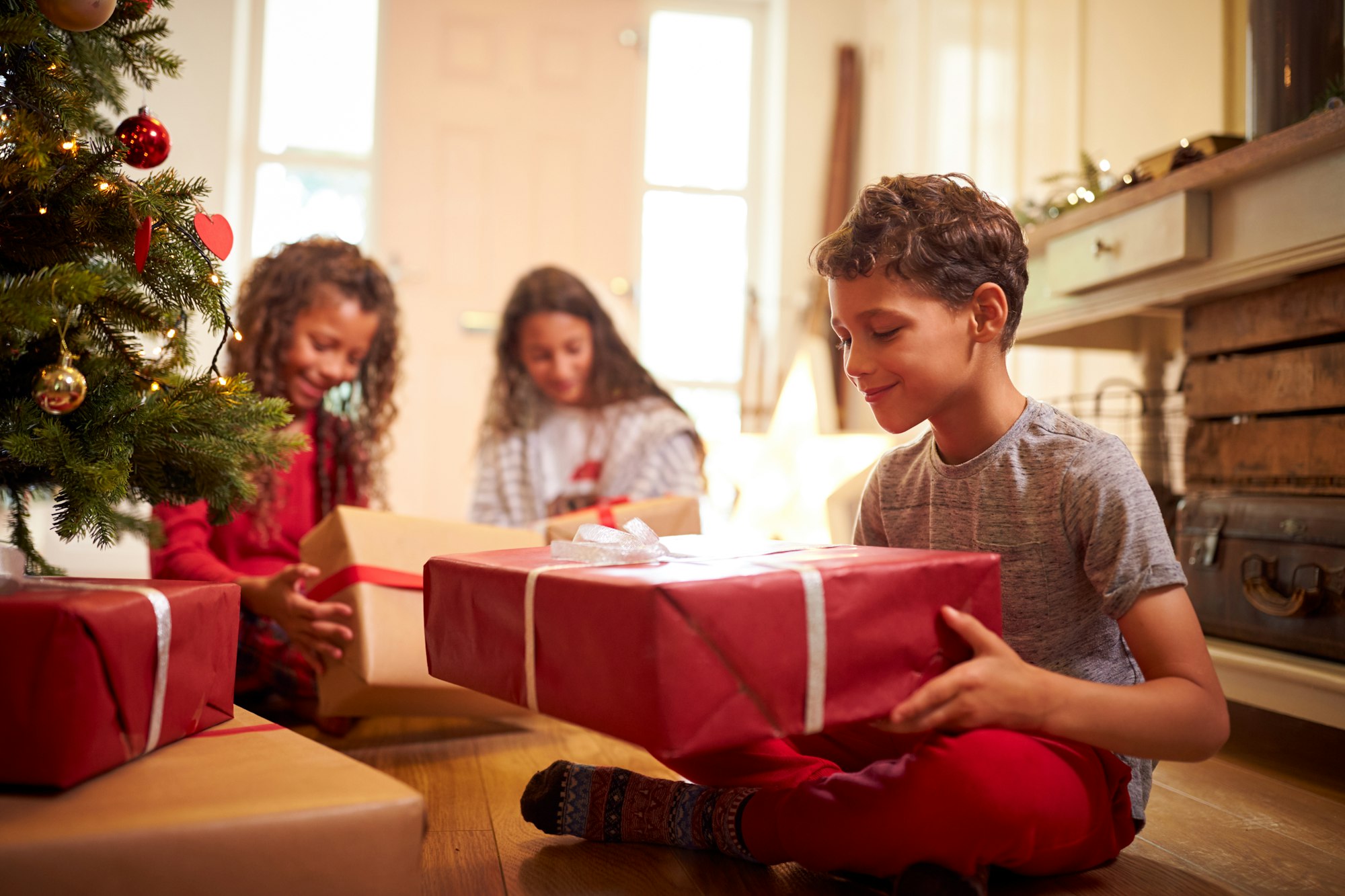 Excited Children Opening Presents By Tree On Christmas Morning