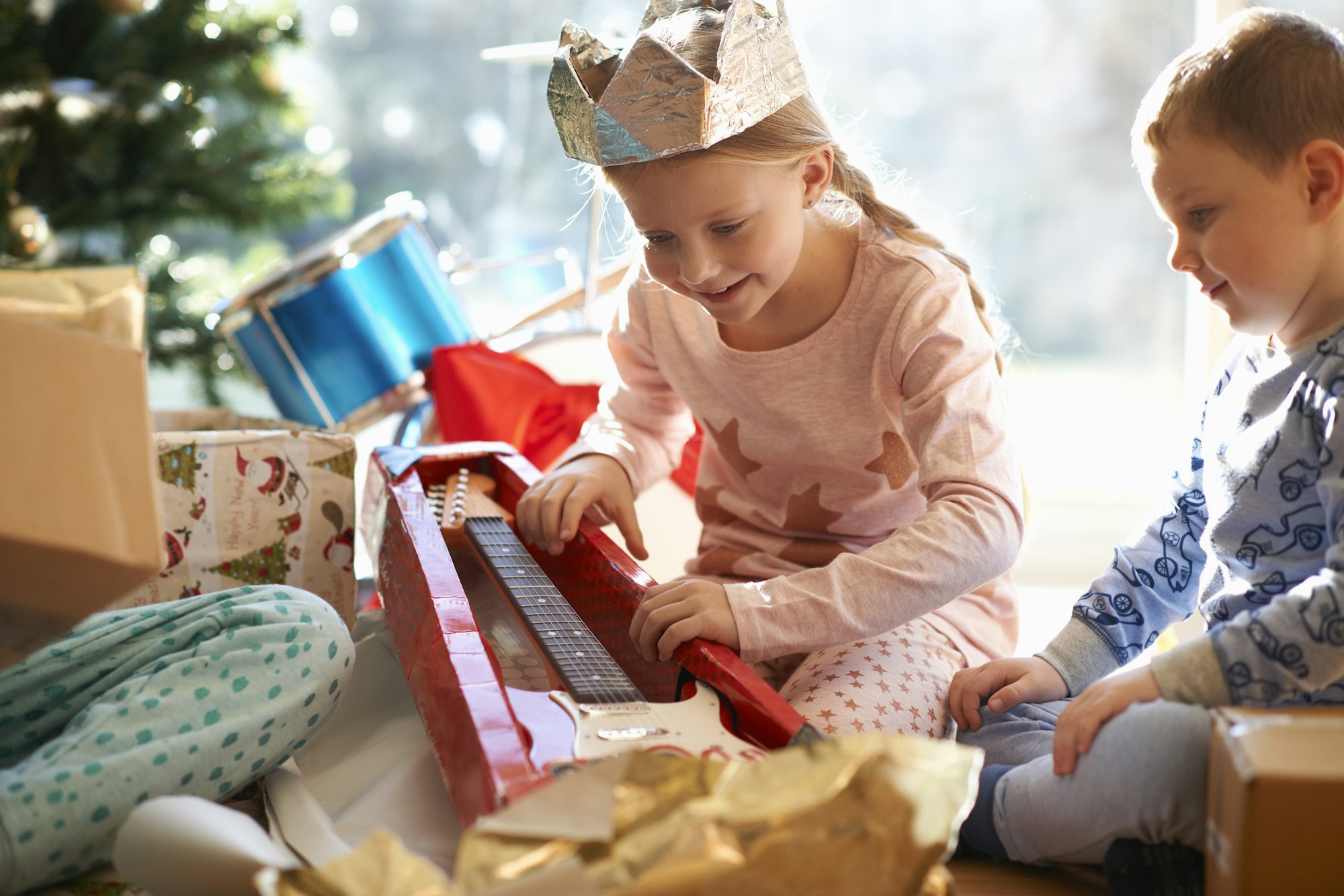 Girl and brother on living room floor gazing at toy guitar christmas gift